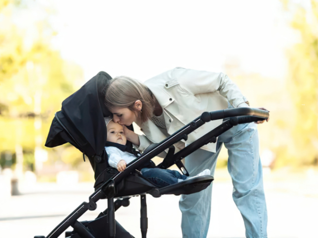 parent leaning over baby to lift it out of a pram - demonstrating back care with a newborn